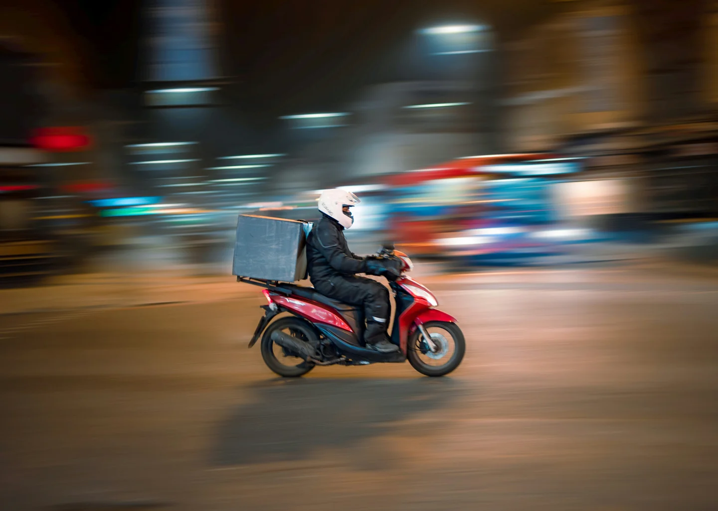 A delivery worker riding a scooter through the city at night